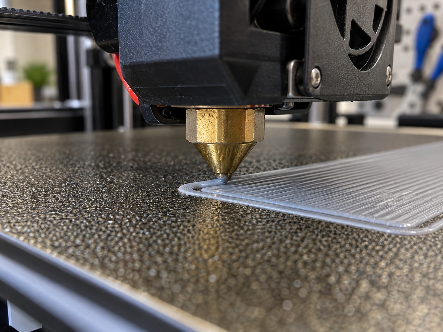 Close-up of a 3D printer nozzle laying down a clean first layer on a textured PEI build plate.